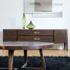 A modern living room scene featuring a wooden sideboard with decorative vases and a coffee table in the foreground. Produktbild-Vorschau
