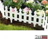 A white picket fence bordering a garden bed with flowers and grass. Produktbild-Vorschau