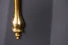 A close-up of a decorative gold metal object mounted on a dark gray wall. Produktbild-Vorschau