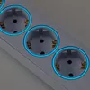 A close-up view of a white power strip with multiple illuminated blue electrical outlets. Produktbild-Vorschau