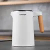 A white electric kettle with a wooden handle sits on a dark countertop in a kitchen setting. Produktbild-Vorschau