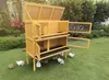 A multi-level yellow wooden rabbit hutch is set up on a green lawn, surrounded by several rabbits. Náhľad obrázku produktu