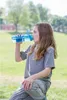 A young person drinking from a water bottle outdoors. Produktbild-Vorschau