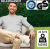 A man sitting on a polyrattan garden chair in a garden setting. Produktbild-Vorschau