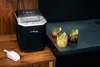 An ice maker on a wooden surface next to three cocktails on a dark countertop. Podgląd zdjęcia produktu