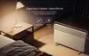 A heater is placed on the floor next to a nightstand with a lamp and a glass of water in a bedroom setting. Produktbild-Vorschau