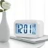 A white digital alarm clock is placed on a book next to a white vase with a white rose. Voir les images du produit