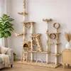 A large cat tree with multiple levels, platforms, tunnels, and scratching posts, set up in a living room environment next to a sofa and a plant. Náhľad obrázku produktu