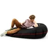 A young person is lying on a black beanbag chair, holding a remote and a magazine. Podgląd zdjęcia produktu