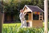 A young girl is playing in a wooden playhouse in a garden. Produktbild-Vorschau