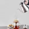 A hand pours hot water from a gooseneck kettle into a pour-over coffee maker, with a cupcake and coffee beans nearby. Produktbild-Vorschau
