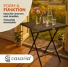 A small square table with drinks and flowers on it, placed on a wooden deck with plants and a garden in the background. Produktbild-Vorschau
