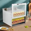 A stainless steel food dehydrator filled with various dried fruits and vegetables, placed on a wooden countertop. Podgląd zdjęcia produktu