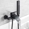 A black bathtub faucet with a waterfall spout and a handheld showerhead is mounted on a white brick wall above a bathtub. Náhled obrázku produktu