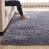 A person's legs and feet wearing slippers are visible, sitting on a sofa next to a plush gray rug. Náhled obrázku produktu