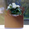 A potted plant with white roses sits in a decorative planter with a fairy motif, placed outdoors on a table. Produktbild-Vorschau