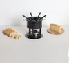 A black fondue set is displayed on a textured tablecloth, with a loaf of bread and a slice of cheese on wooden plates. Podgląd zdjęcia produktu