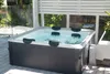 A hot tub is situated on a wooden deck outdoors, surrounded by greenery and a white slatted fence. Náhľad obrázku produktu