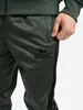 A close-up shot of a person's hand in the pocket of green tracksuit bottoms with a black stripe down the side. Anteprima dell’immagine prodotto