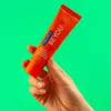 A hand holding an orange tube of Curaprox toothpaste against a bright green background. Anteprima dell’immagine prodotto
