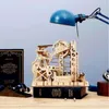 A wooden marble run model is displayed on a desk next to a book and a desk lamp. Voir les images du produit