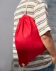 A person wearing a striped t-shirt and jeans is carrying a red drawstring bag over their shoulder. Produktbild-Vorschau