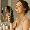 A woman is smiling and holding a black water flosser in a bathroom. Náhľad obrázku produktu