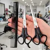 A hand holding a comb and two pairs of scissors in a hair salon. Produktbild-Vorschau
