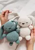 Two crocheted bunnies, one eucalyptus green and one white, are held by a person's hands on a white background. Podgląd zdjęcia produktu