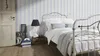 A bedroom scene with a bed, door, and wallpaper. Produktbild-Vorschau