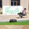 A man sits on a chair in a garden, looking at a smartphone which displays a map of a lawn being mowed by a robot mower. The robot mower is visible on the grass. Produktbild-Vorschau