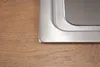 A close-up view of the corner of a stainless steel sink on a wooden countertop. Produktbild-Vorschau