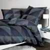 A bed with navy blue bedding featuring a geometric pattern, pillows, and a bedside table with a lamp. Produktbild-Vorschau