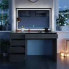 A vanity table with a large illuminated mirror, set in a room at night with a window view of a snowy landscape. Produktbild-Vorschau