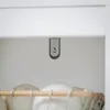 A close-up view of the inside of a cabinet or shelf, showing a metal bracket with a screw attached to the top surface, and the edge of a laundry basket with wooden elements and white items below. Produktbild-Vorschau