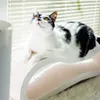 A black and white cat is lying on a scratching post in front of a window with blinds. Produktbild-Vorschau