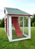 A chicken coop is shown in a grassy outdoor setting with trees and a hill in the background. Produktbild-Vorschau