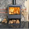 A modern wood-burning stove with a fire burning inside, set against a brick wall. Logs are stacked neatly below the stove. Produktbild-Vorschau