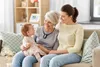 Three generations of women sitting on a couch, with the grandmother wearing a pendant device. Produktbild-Vorschau
