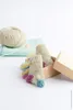 A pair of knitted baby socks with colorful accents, placed in a small cardboard box, with a ball of yarn and knitting needles in the background. Produktbild-Vorschau