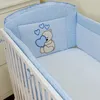 A close-up view of a baby crib with blue and white checkered bedding and a light blue bumper pad featuring an embroidered teddy bear holding a heart. Voir les images du produit