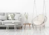 A minimalist living room scene with a gray sofa and a hanging chair. Produktbild-Vorschau