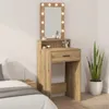 A makeup vanity with a lighted mirror is shown in a bedroom setting next to a bed and a plant. Voir les images du produit