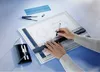 A person's hands are shown drawing on a drafting table with a technical drawing. Anteprima dell’immagine prodotto