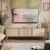 A living room scene featuring a TV stand with a TV mounted above it, decorated with artwork and plants. Produktbild-Vorschau