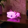 A pink pixelated axolotl lamp is lit up on a wooden shelf, with a plant in a pot to the left and a speaker to the right. Anteprima dell’immagine prodotto