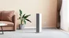 A modern living room with a sofa, plant, and a white and gray electric heater. Voir les images du produit