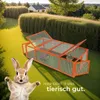 A rabbit hutch is set up on a green lawn in a garden, with a cartoonish rabbit in the foreground. The text "HIER GEHT'S UNS tierisch gut." is visible. Produktbild-Vorschau
