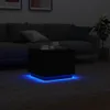 A black coffee table with blue LED lights is placed on a gray rug in a dimly lit living room, with a sofa in the background. Produktbild-Vorschau