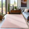 A living room with a pink rug, sofa, and wooden furniture, with plants and a window view. Produktbild-Vorschau
